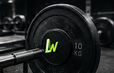 A black 10 kg weight plate on a barbell in a dark gym, with the loadwise monogram on the plate